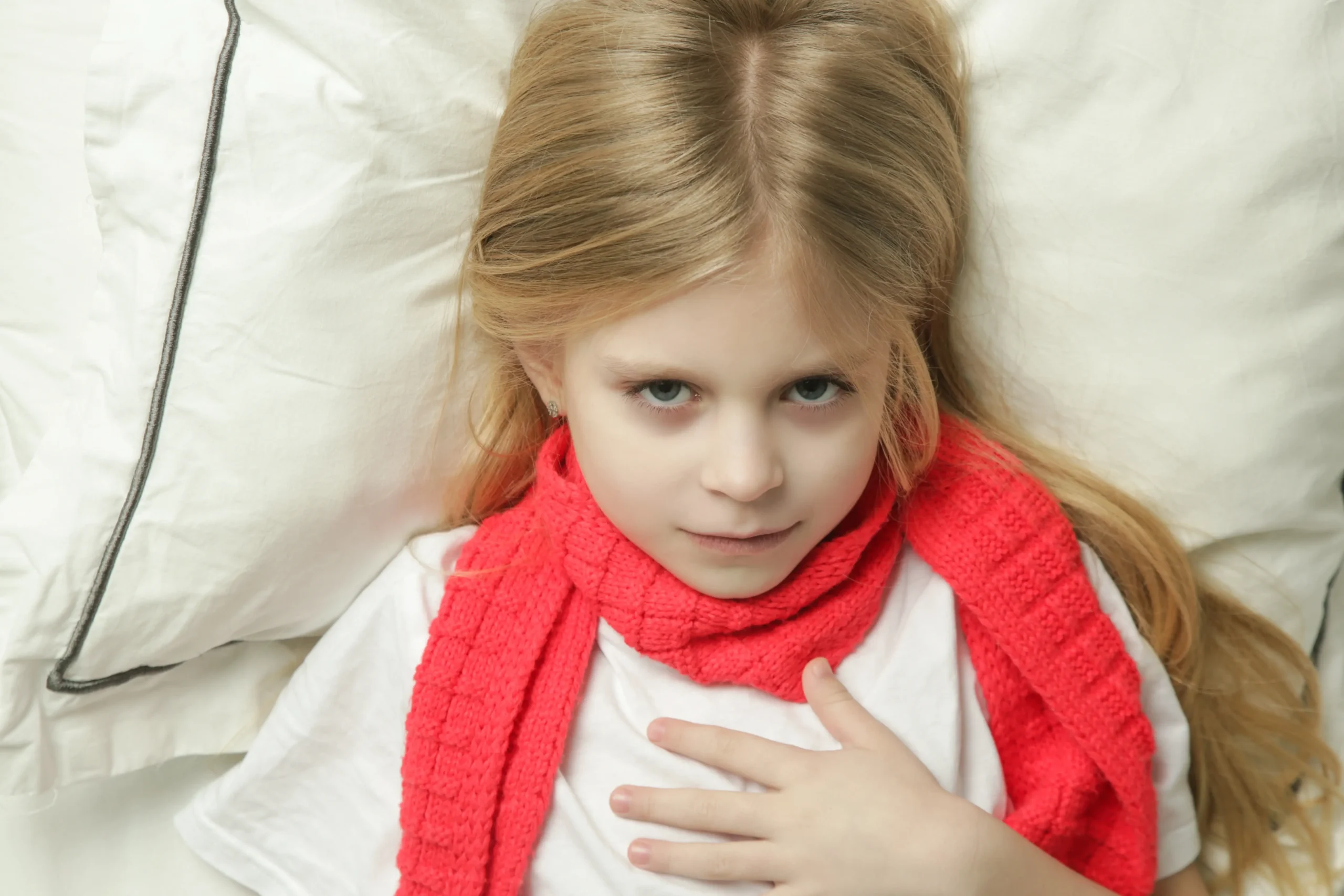 Kislány piros sállal, torokfájás miatt a mellkasát érinti.
